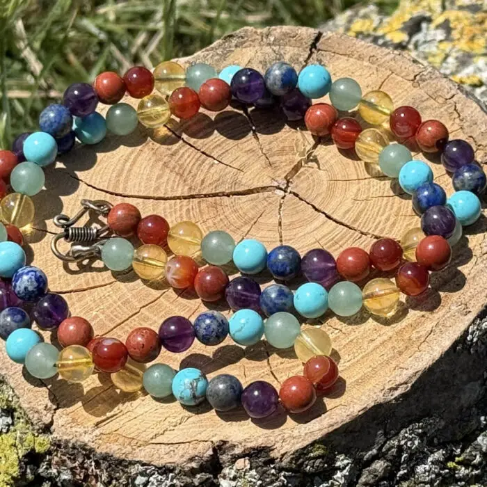 7 Chakra Necklace placed on wooden block in garden with grass background
