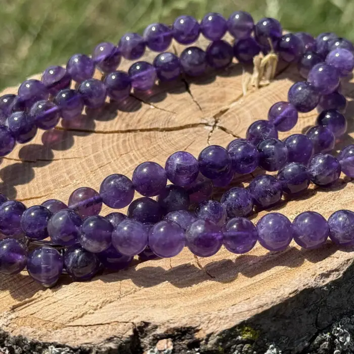 Amethyst crystal necklace placed on a wooden block with a garden background of grass and greenery.