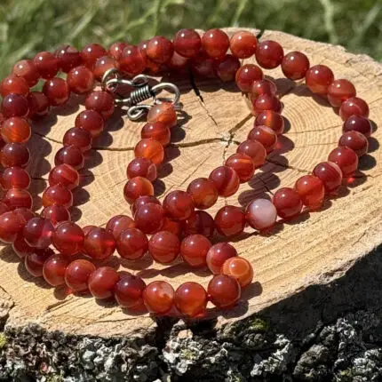 Carnelian crystal necklace resting on a wooden block with a garden background of green grass and foliage.