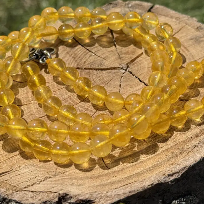 Citrine crystal necklace placed on a wooden block with a garden background of green grass and foliage.