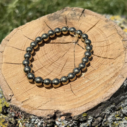 Golden pyrite crystal bracelet placed on a wooden block with a blurred garden background.