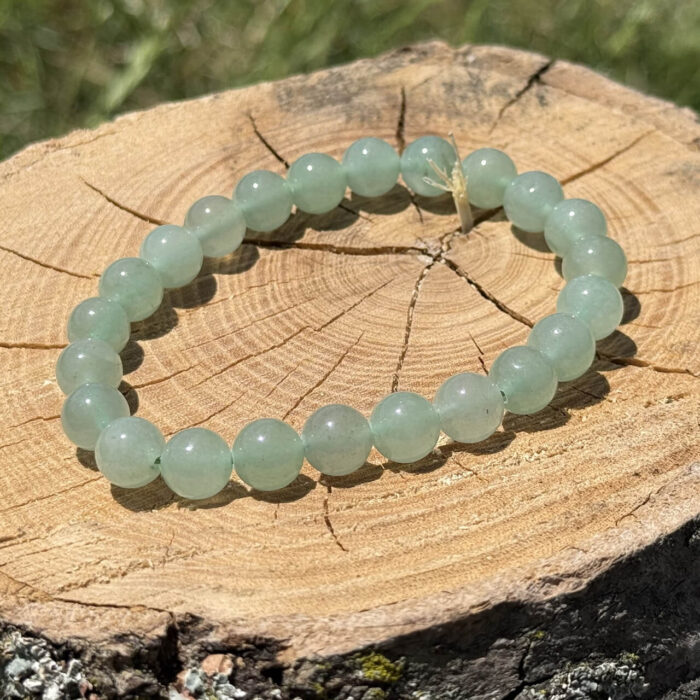 Green aventurine crystal bracelet placed on a wooden block with a blurred garden background.