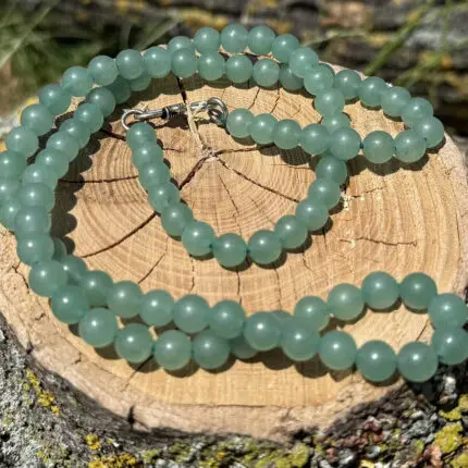 Green aventurine crystal necklace placed on a wooden block with a garden background of grass and greenery.