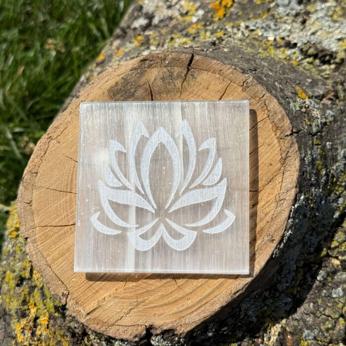Front-facing image of a lotus design Selenite charging plate placed on a wooden block with engraved details