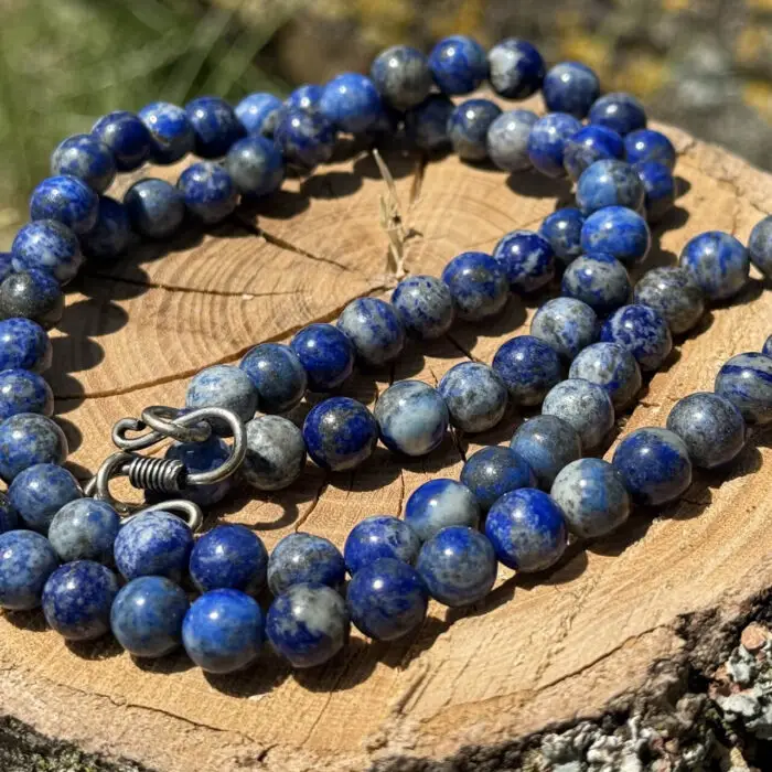 Lapis lazuli crystal necklace placed on a wooden block with a garden background of grass and greenery.