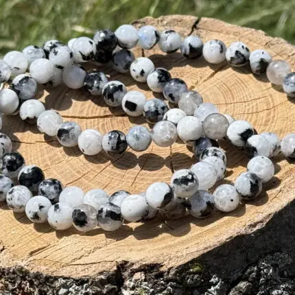 Moonstone crystal necklace placed on a wooden block with a garden background of green grass and plants.
