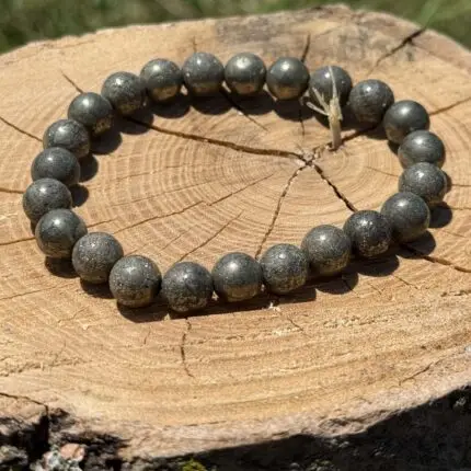 Real Natural Pyrite Crystal Bracelet made of metallic golden-grey beads, displayed on a wooden log under natural sunlight.