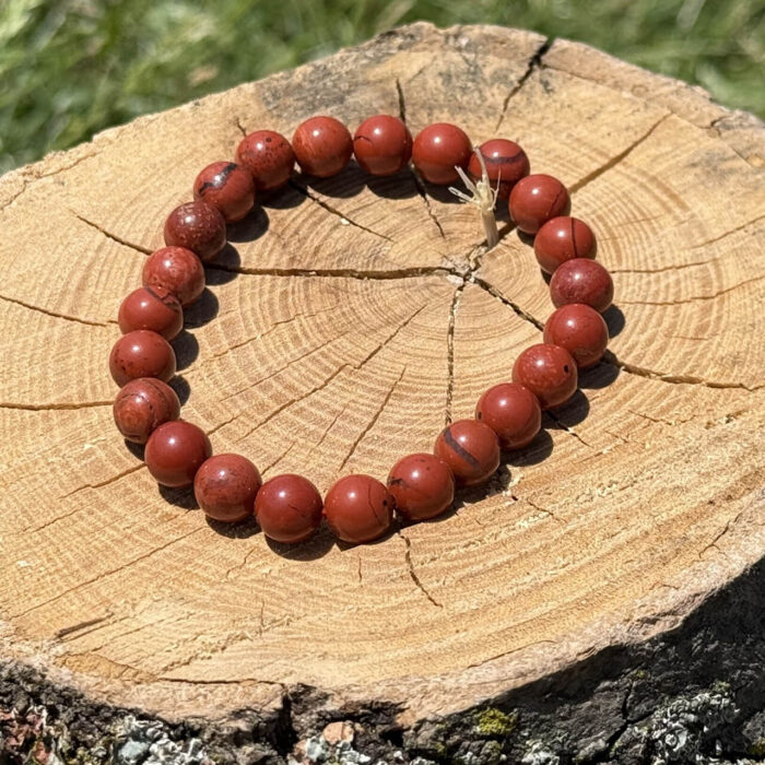 Red jasper crystal bracelet placed on a wooden block with a blurred garden background.