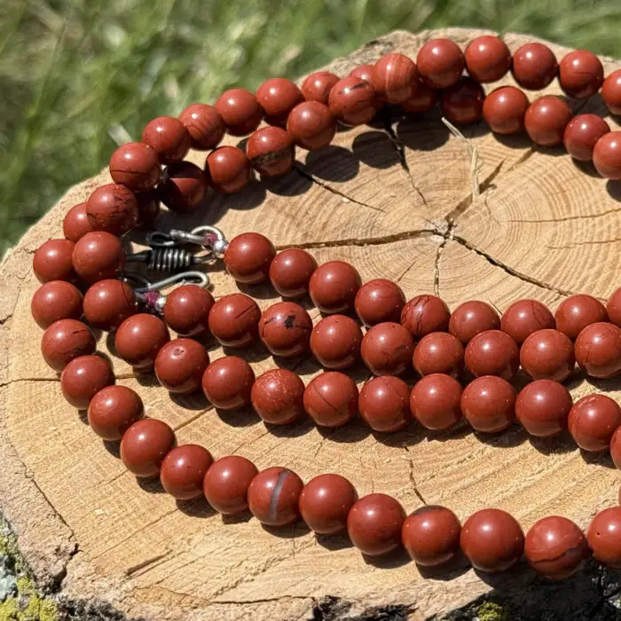Red jasper crystal necklace placed on a wooden block with a garden background of green grass and foliage.