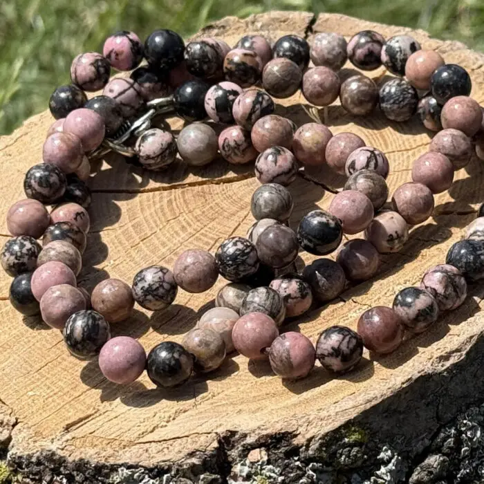 Rhodonite crystal necklace placed on a wooden block with a garden background showing grass and greenery.