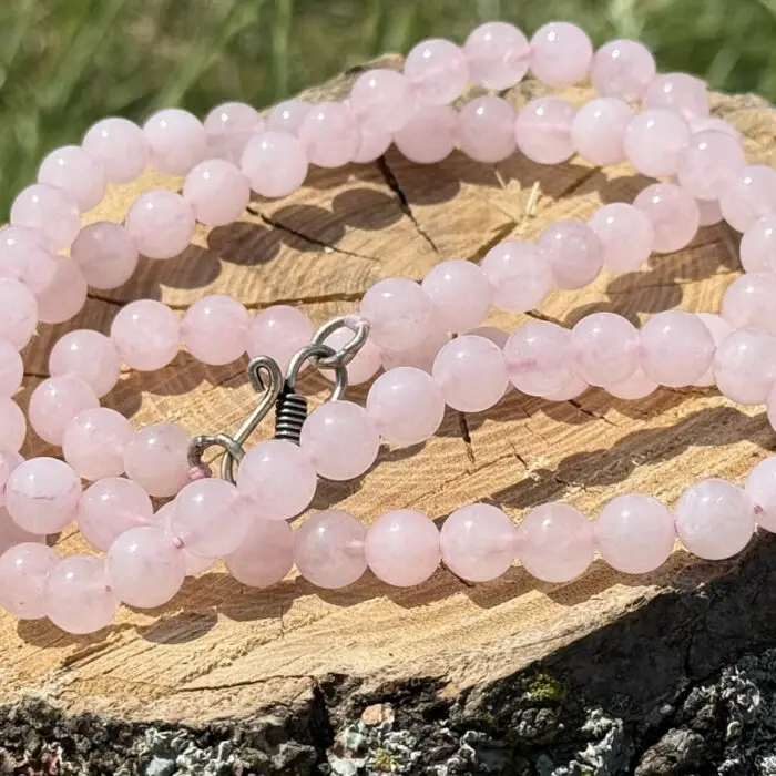 Rose quartz necklace displayed on a wooden block with a garden background of grass and greenery.
